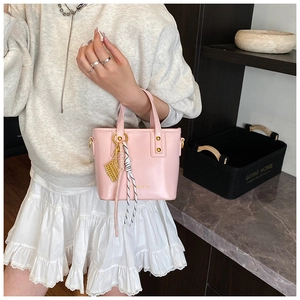 Detail of light pink PU leather bucket bag with gold geometric tag and woven tassel