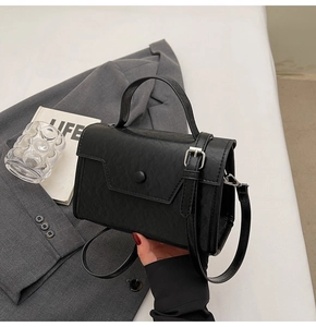 Detail of black crossbody bag showing pebbled leather texture and round decorative buckle