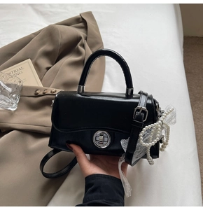 Detail of black faux leather mini square bag with silver lock and pearl bow charm
