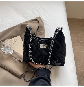 Detail of black patent leather quilted bag with silver chain and turn-lock closure