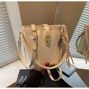 Détail du sac seau crème montrant la texture du cuir, fermoir doré et pendentif tressé