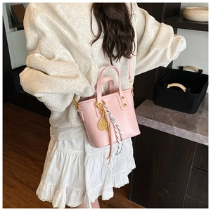 Chic light pink bucket bag worn with white sweater and ruffled skirt for daily style