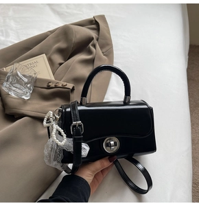 Detail of black glossy handbag with silver rotary buckle and lace pearl pendant decor