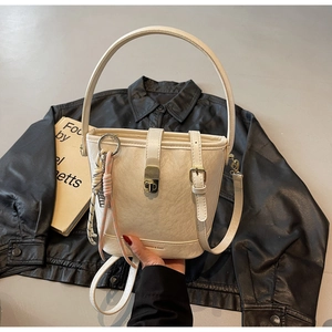 Détail du sac seau crème avec texture cuir litchi et breloque tressée colorée