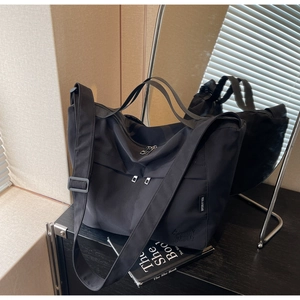 Detail of black nylon tote bag showing the side brand label and durable shoulder strap