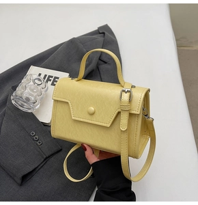 Detail of light yellow leather crossbody bag with top handle and adjustable shoulder strap