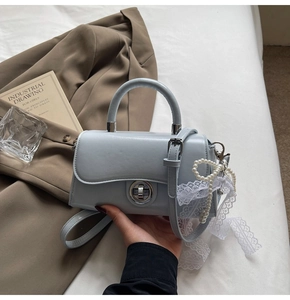 Detail of light blue crossbody bag with round metal lock, pearl charm and lace ribbon