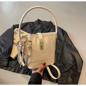 Détail du sac seau crème montrant le fermoir en métal, la poignée et le charme tissé