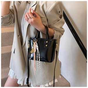 Detail of black glossy bucket bag with gold lettering and decorative knot charm