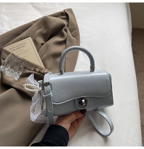 Close-up of light blue small square crossbody bag with pearl and lace pendant details