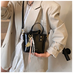 Detail of black mini bucket bag with gold tennis racket charm and tassel accent