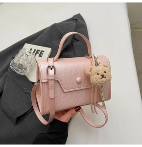 Close-up of pink pebbled leather small square bag with cute white teddy bear charm accessory