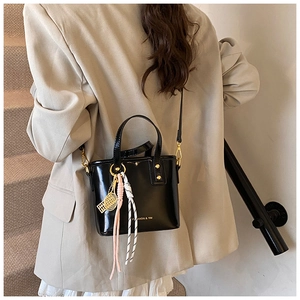 Detail of glossy black patent leather bucket bag with gold hardware and tennis charm