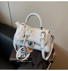 Close-up of light blue leather handbag featuring a silver twist lock and pearl lace detail