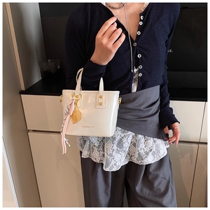 Close-up of cream mini tote with glossy finish and decorative tennis racket charm