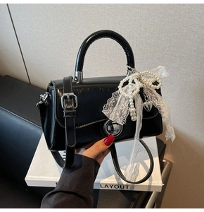 Detail of black patent leather handbag featuring pearl lace bow and silver heart charm