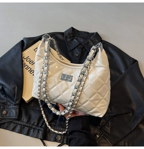 Close-up of white quilted diamond pattern bag on black leather with silver chain strap