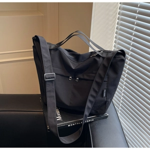 Detail of black large-capacity tote bag with adjustable strap on a leather sofa