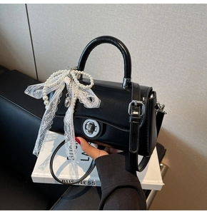 Close-up of black patent leather handbag with pearl and lace bow charm detail