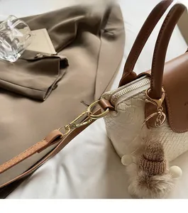 Détail de la texture tissée crème et du cuir marron du sac avec accessoires dorés