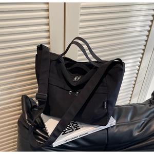 Close-up of black nylon tote bag with dual front zipper pockets and wide shoulder strap