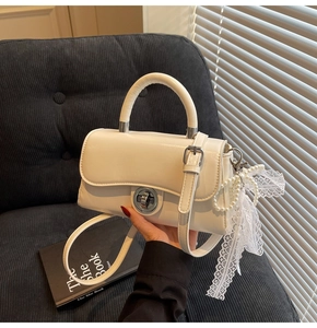 Detail of cream crossbody bag featuring a silver twist lock and pearl lace bow charm