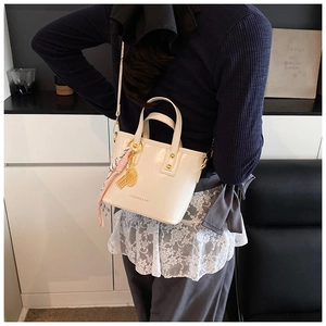 Detail of cream white leather bucket bag with silk scarf and gold tennis racket pendant