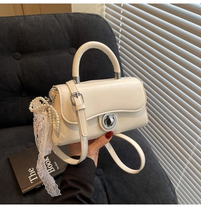 Detail of cream crossbody bag with silver lock and decorative pearl lace charm
