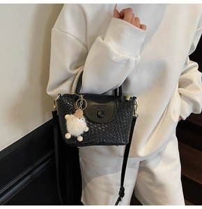 Detail der schwarzen geflochtenen Handtasche mit Metallschnalle und Plüschtier-Anhänger