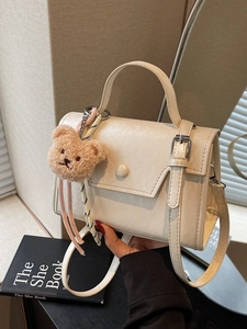 Cream square handbag with plush bear charm and shoulder strap in casual setting