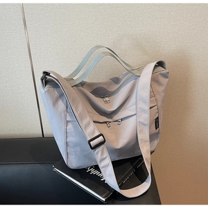 Close-up of light grey-blue nylon tote bag with multi-zipper pockets on a dark sofa