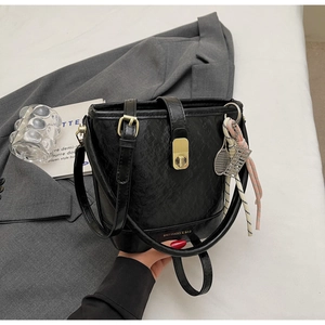Détail d'un sac seau noir en PU avec ferrures dorées, breloque de tennis et ruban soyeux