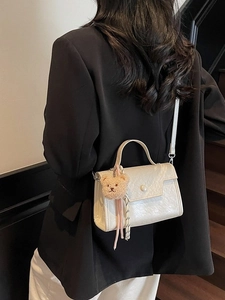 Chic beige textured faux leather crossbody bag with pearl clasp and bear charm on model