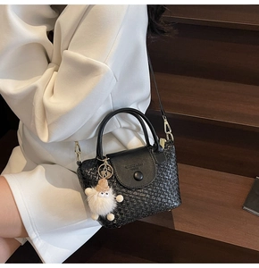 Détail d'un sac à main noir à texture tressée avec une peluche sur la bandoulière