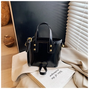 Detail of black glossy handbag with gold studs and FASHION & YM logo in soft light