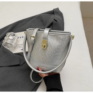 Détail d'un sac seau argenté avec fermoir doré rotatif et texture de cuir métallisé plissé