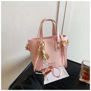 Pink bucket bag detail with golden hardware and fashion charm on textured desk