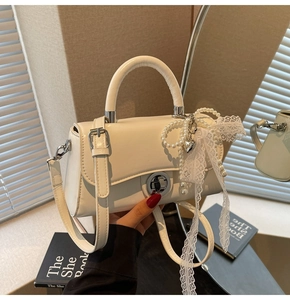 Close-up of white crossbody bag with pearl chain and lace bow on indoor background
