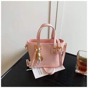 Pink mini tote bag with gold racquet charm and adjustable strap on a dark tabletop