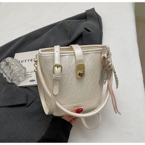 Détail du sac seau crème avec texture plissée perlée et pendentif de raquette de tennis