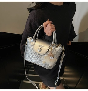 Detail einer silbernen Flecht-Handtasche mit rundem Griff und Plüsch-Anhänger