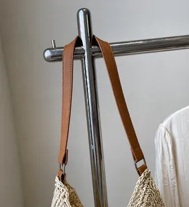 Dettaglio dei lunghi manici in similpelle marrone su una borsa shopping in paglia beige