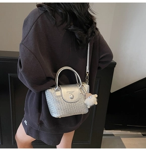 Detail einer silbernen gewebten Handtasche mit Plüschanhänger und Leder in Metalloptik