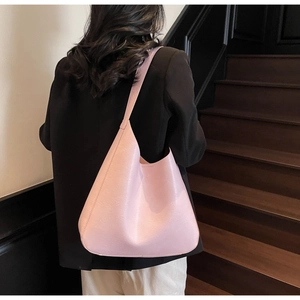 Sac à épaule minimaliste en cuir rose avec large bandoulière porté par un mannequin