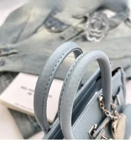 Dettaglio borsa azzurra in pelle martellata con hardware argentato e ciondolo a forma di cuore