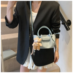 Mini sac seau bleu clair tissé avec pendentif ours porté par un mannequin sur un escalier
