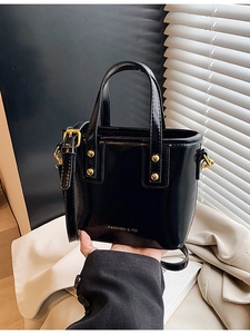 Elegant black glossy bucket bag with golden studs and fashion logo on the front
