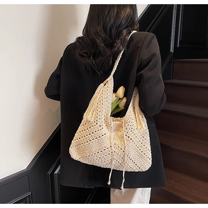 Detail of crochet straw beach bag with hollow weave pattern and tassel charm