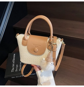 Detail einer geflochtenen Handtasche mit Ledergriffen und Plüsch-Pompon-Zubehör