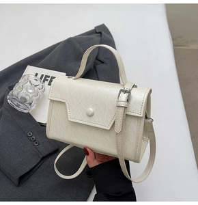 Detail of a cream leather crossbody bag featuring a textured flap and stylish metal buckle